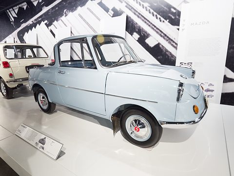 Pale blue small coupé on a white plinth in a bright gallery with graphic black-and-white walls. Opens a larger view