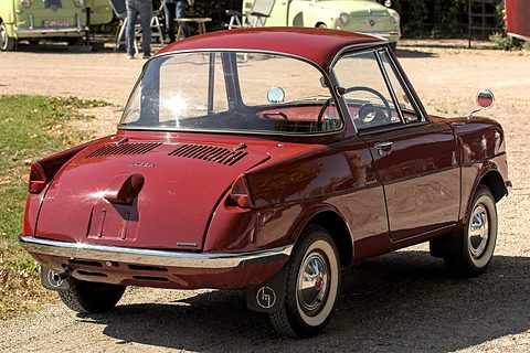Rear three-quarter of a maroon coupé with louvred engine lid, on gravel by grass. Opens a larger view
