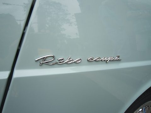 Chrome handwritten-style R360 coupe script on pale blue paint beside a door shut line. Opens a larger view