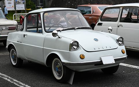 White small coupé with whitewall tyres and a blanked plate, parked beside other old cars. Opens a larger view