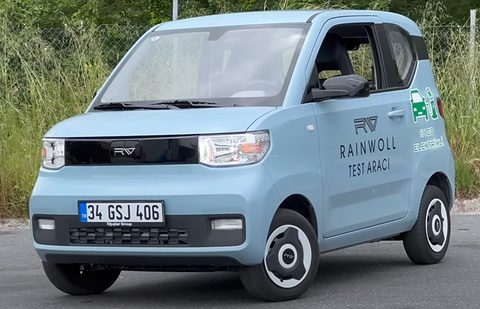 Pale blue boxy city car with Rainwoll Test Aracı lettering and a Turkish plate, parked by long grass. Opens a larger view