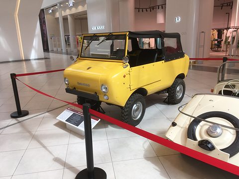 Yellow miniature off-roader with a black soft top and chunky tyres, seen from the front left inside a red-roped display.