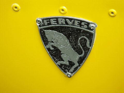 Shield-shaped black and silver badge reading FERVES with a leaping bull, fixed to yellow bodywork by rivets. Opens a larger view