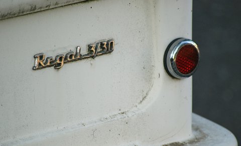 Chrome script lettering and a round red reflector on weathered white bodywork. Opens a larger view