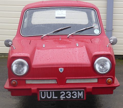 Red three-wheel saloon facing the camera, round headlamps and a single centre badge. Opens a larger view