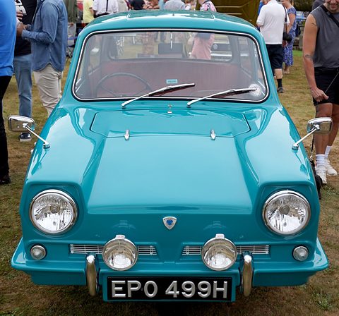 Turquoise three-wheeler facing the camera with chrome bumper, twin spot lamps and mirrors. Opens a larger view