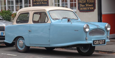 Pale blue three-wheel saloon with a cream roof parked in a street outside a pub. Opens a larger view