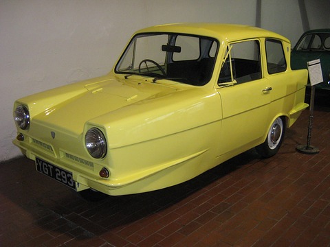 Yellow three-wheel saloon with round headlamps on a brick museum floor. Opens a larger view