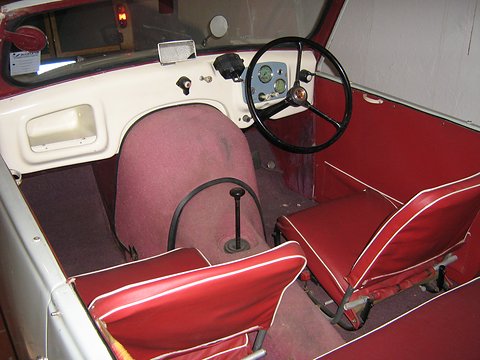 Open cockpit with red seats, a black steering wheel, green-faced dials and a white dash. Opens a larger view