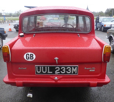 Rear of a rain-spotted red three-wheeler with a GB sticker and chrome script. Opens a larger view