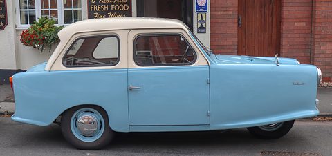 Pale blue and cream three-wheel saloon in side view against a brick building. Opens a larger view