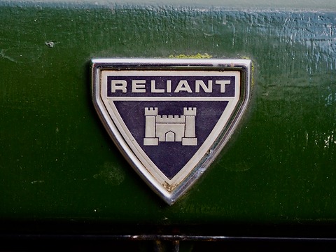 Shield-shaped chrome badge with the word Reliant above a castle, on green paintwork. Opens a larger view