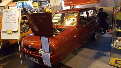 Bronze-orange hatchback with its bonnet raised and notices in the windows on a busy stand. Opens a larger view