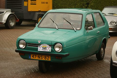 Turquoise-green small hatchback with round headlamps and a rally plaque, parked on brick paving. Opens a larger view
