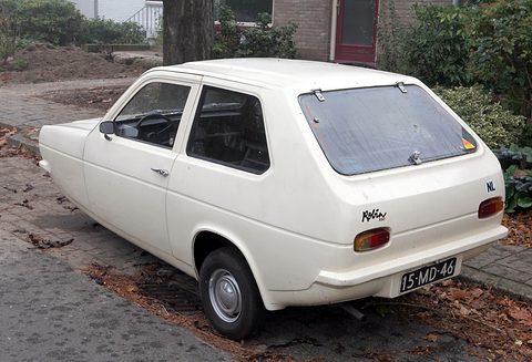White hatchback from behind, NL sticker and Dutch plate, parked by fallen leaves on paving. Opens a larger view