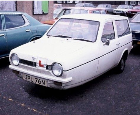 A white three-wheeled hatchback with round headlamps and a red L-plate, parked between other 1970s cars.