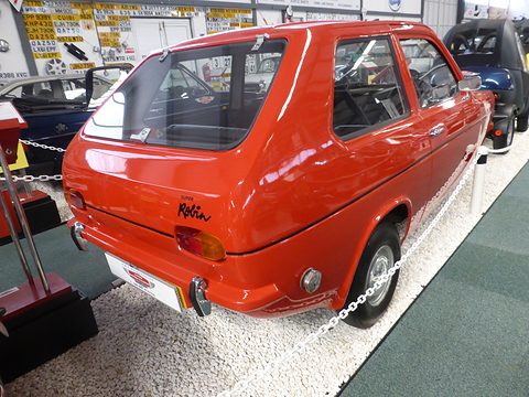 Red hatchback from the rear quarter with Robin script on the tail, standing on white gravel. Opens a larger view