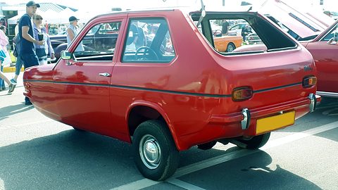 Red hatchback from the rear quarter with its rear glass open, show visitors behind.
