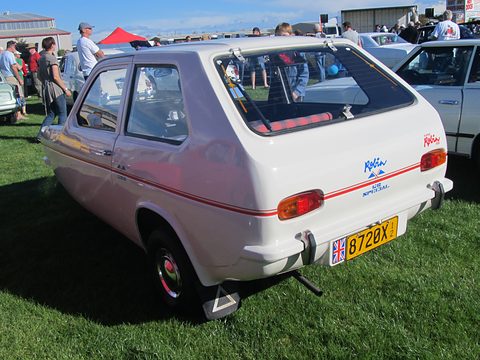 White hatchback seen from behind on grass, with blue Robin script and a yellow number plate. Opens a larger view