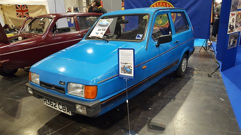 Bright blue hatchback with an information board on a show stand, a maroon Robin behind. Opens a larger view