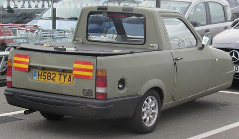 Olive pick-up from behind with striped reflective panels and a tonneau cover, trolleys behind. Opens a larger view