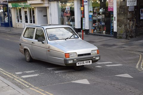 Silver hatchback with orange indicators turning across a town street past shopfronts. Opens a larger view