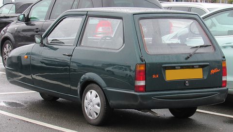 Dark-green hatchback from the rear quarter on a rain-wet car park. Opens a larger view