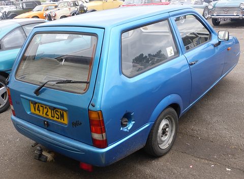 Blue hatchback seen from behind on tarmac, other show cars parked around it. Opens a larger view