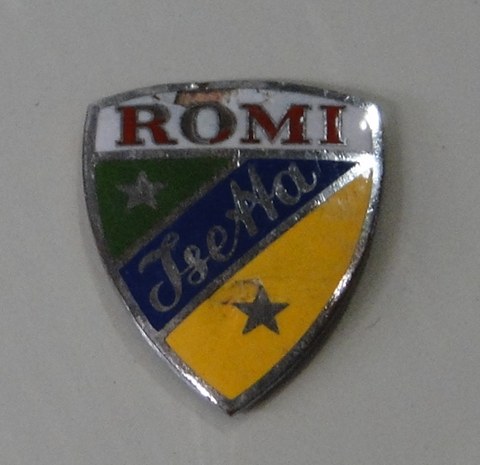 Chrome-edged shield badge with ROMI in red over green, blue and yellow fields, Isetta in script and two stars.
