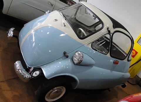 Close front quarter of a pale blue and white bubble car with its front door swung open and a chrome bumper, in a museum.