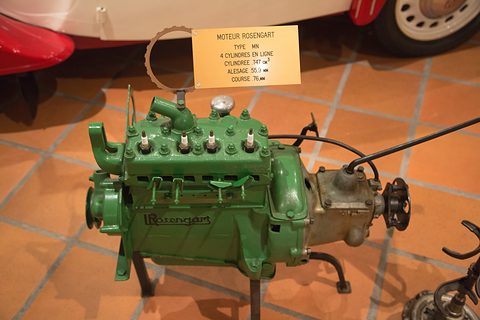 A green four-cylinder engine with its gearbox on a stand, a printed card labelled Moteur Rosengart above it. Opens a larger view