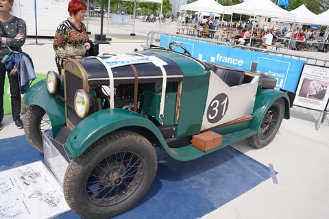 A green and black open two-seat racer with wire wheels and the number 31 on its tail, parked on blue matting. Opens a larger view