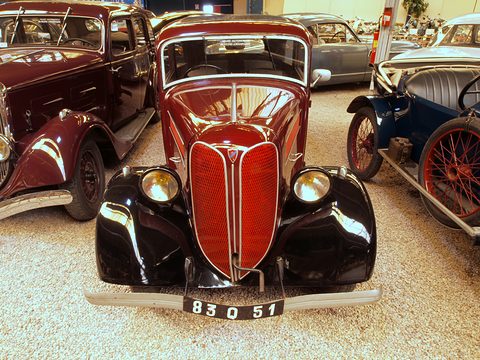 The front of a red saloon with a tall split V-shaped grille, black wings and two chrome headlamps. Opens a larger view