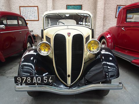 The front of a cream car with a tall black split grille, yellow headlamps, black wings and a chrome bumper. Opens a larger view
