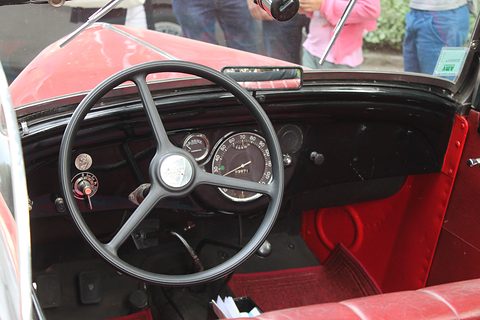 A painted dashboard with two round dials behind a large three-spoke steering wheel, red seats below. Opens a larger view