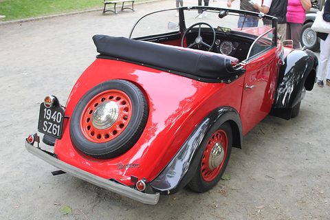 The rear of a red open car with a spare wheel on the tail and a folded black hood. Opens a larger view