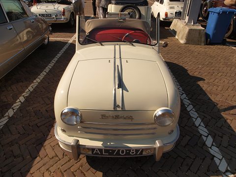 Cream open two-seater facing the camera with round headlamps, R de Rovin script and slatted grille. Opens a larger view