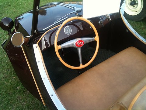 Looking into a brown open car at a cream steering wheel with a red Rovin badge and a tan bench seat.