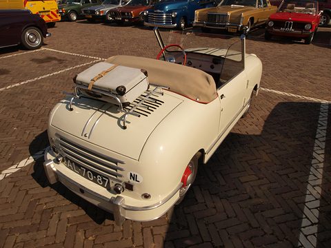 Cream open two-seater seen from behind with a suitcase strapped to a chrome rack over slatted vents. Opens a larger view