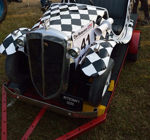 Chequered miniature car seen from the front on a red trailer, chrome grille and twin lamps, rally plate 41. Opens a larger view