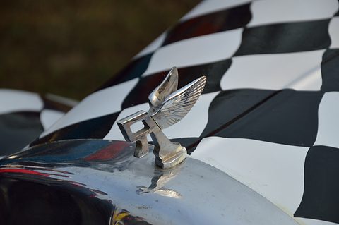Chrome winged mascot on a radiator cap, black and white chequered paint curving behind it. Opens a larger view