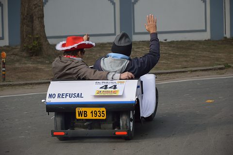 Rear of a white miniature car lettered NO REFUSAL with plate WB 1935, two occupants seen from behind, one waving. Opens a larger view