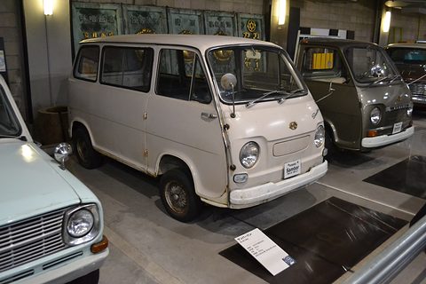 Cream small cab-over van with chrome bumpers in a dim museum, another small van behind. Opens a larger view