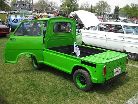 Rear of a bright green small pick-up with an open door and a flag in its bed on grass. Opens a larger view