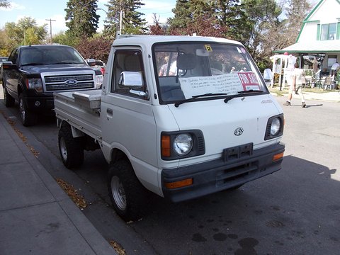 White small cab-over truck with a sale sign in the windscreen parked on a residential street. Opens a larger view