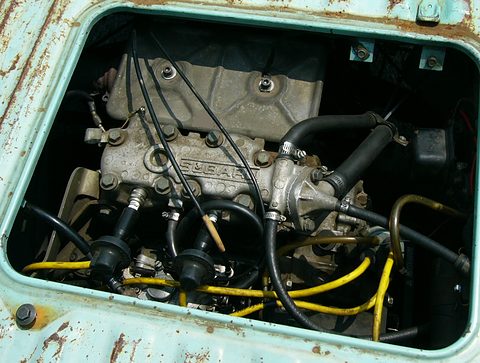 Close view of a small engine with spark-plug leads and yellow wires through a rusty hatch.