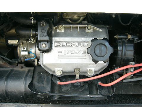 Close view of a small engine cover reading ‘Subaru 3 valve’ with red hoses beside it. Opens a larger view