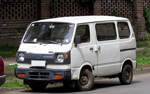 White small cab-over van with dark bumpers parked by a brick wall with patterned openings. Opens a larger view