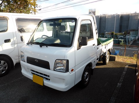 White small cab-over truck with a yellow plate parked beside a white van.