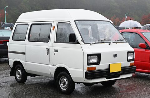 White high-roof small van with a yellow plate on wet tarmac beside a red car. Opens a larger view